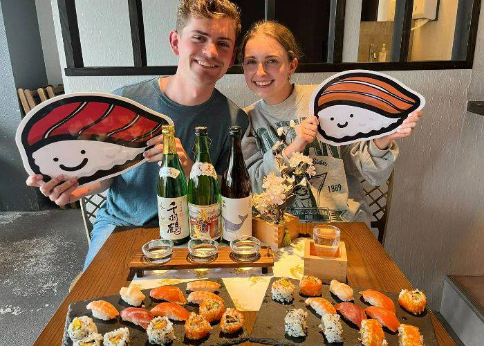 Two guests flying in front of their handmade sushi and cups of sake.